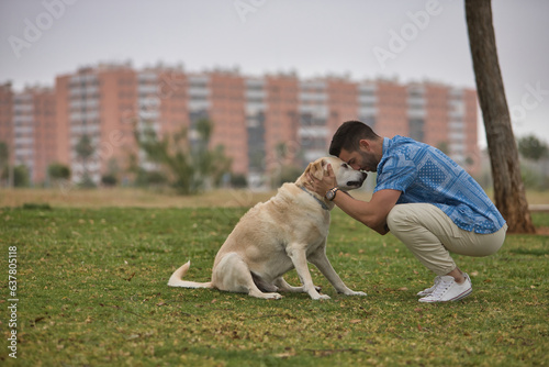 Young Hispanic man, crouching on the grass joining his forehead with his dog's forehead in loving and tender attitude. Concept, dogs, pets, animals, friends.
