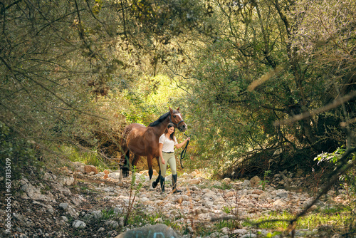 Horsewoman walking with chestnut horse in woods