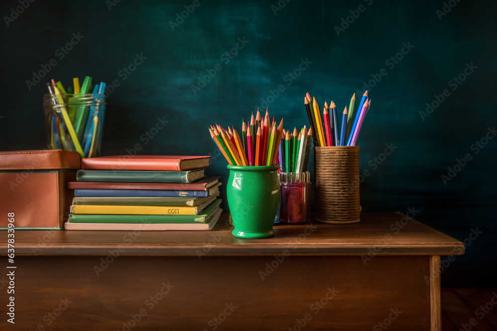 Books stacked and a red app on the top of that, colored pencils in a holder cup on a wooden table