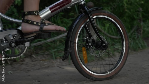 Close-up of a woman's legs in black sandals on a bicycle alone in a summer park near the sea. Sunny day, sand and grass. Unrecognizable girl on a bike, healthy lifestyle, aesthetic footage.