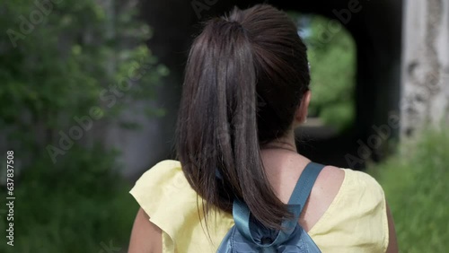 Young brown hair woman with backpack riding bicycle on park, back view. Camera moving forward after her, slow motion effect