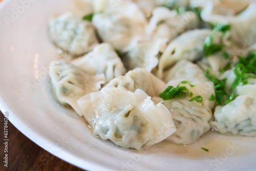 Fresh, delicious boiled garlic chives dumplings, jiaozi in white plate on wooden table background.