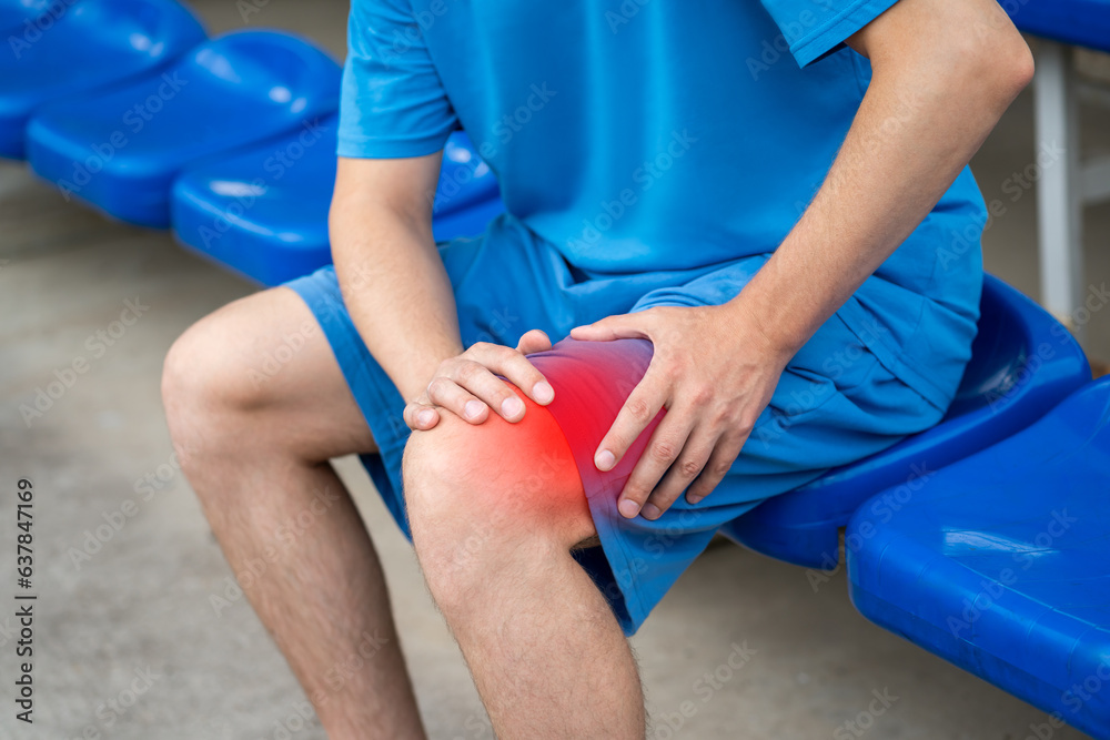 Diseases of the knee joint, bone fracture and inflammation, athletic man on a sports ground after workout suffering from pain in leg and doing self-massage