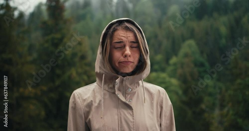 A sad blonde girl stands against the background of forest rain in the mountains, she is sad and looks at the camera