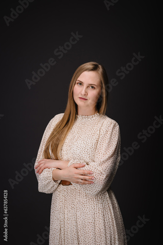 Young serious woman with crossed arms isolated on black wall with copy space. Beautiful girl with folded hands looking at camera. Closeup portrait of lady in dress looks confident on black background.