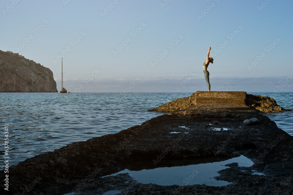 Slim woman doing yoga on rocky seashore