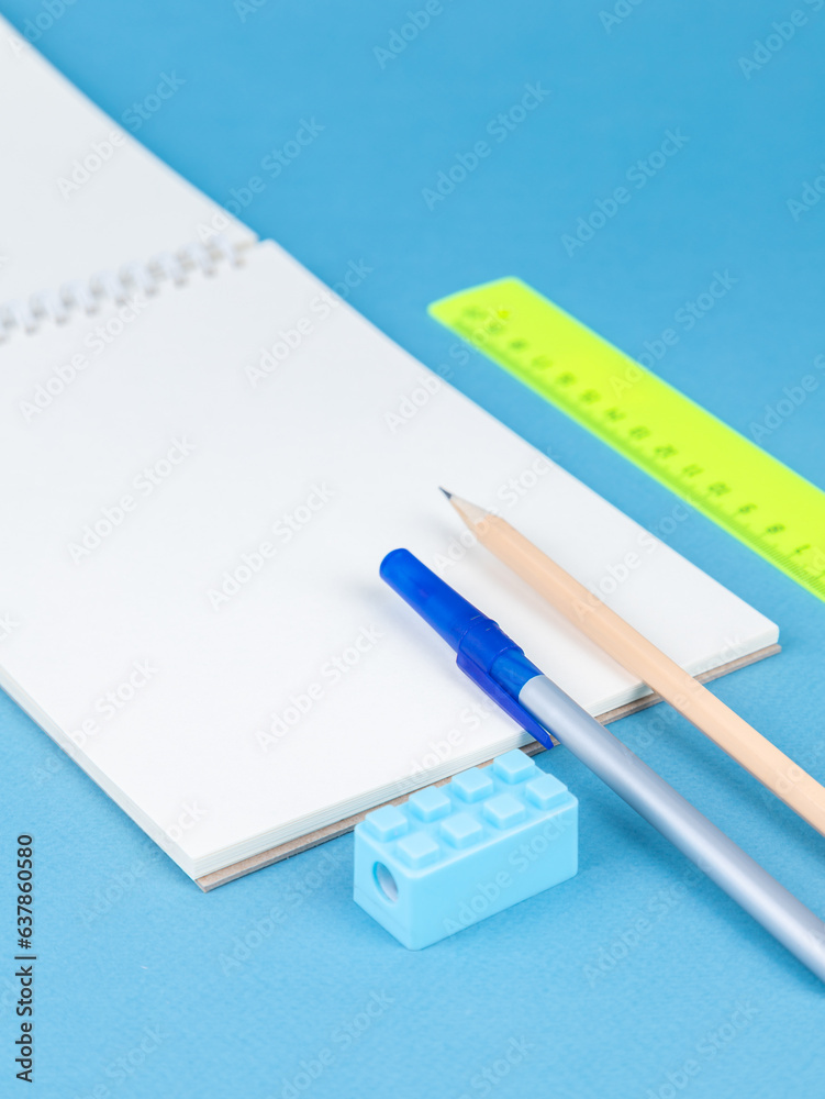 close-up of a paper notebook with blank sheets, a pen, a pencil and a paper clip on a blue background close-up of a paper notebook with blank sheets, a pen, a pencil and a paper clip on a blue background