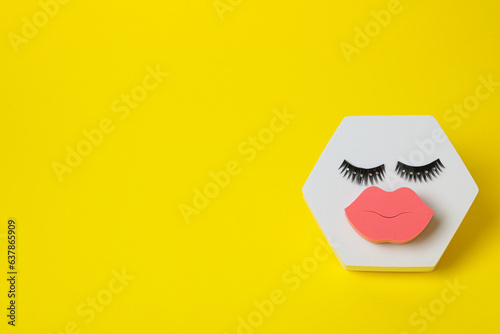 Cosmetic sponge and false eyelashes on yellow background, space for text