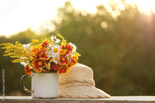 cup with flowers and braided hat in garden, natural abstract sunny background. summer season. rustic composition with flowers. relax time. copy space. template for design