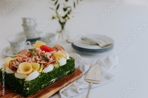 Swedish sandwich cake with shrimps, cheese, ham and eggs on wooden board at table photo