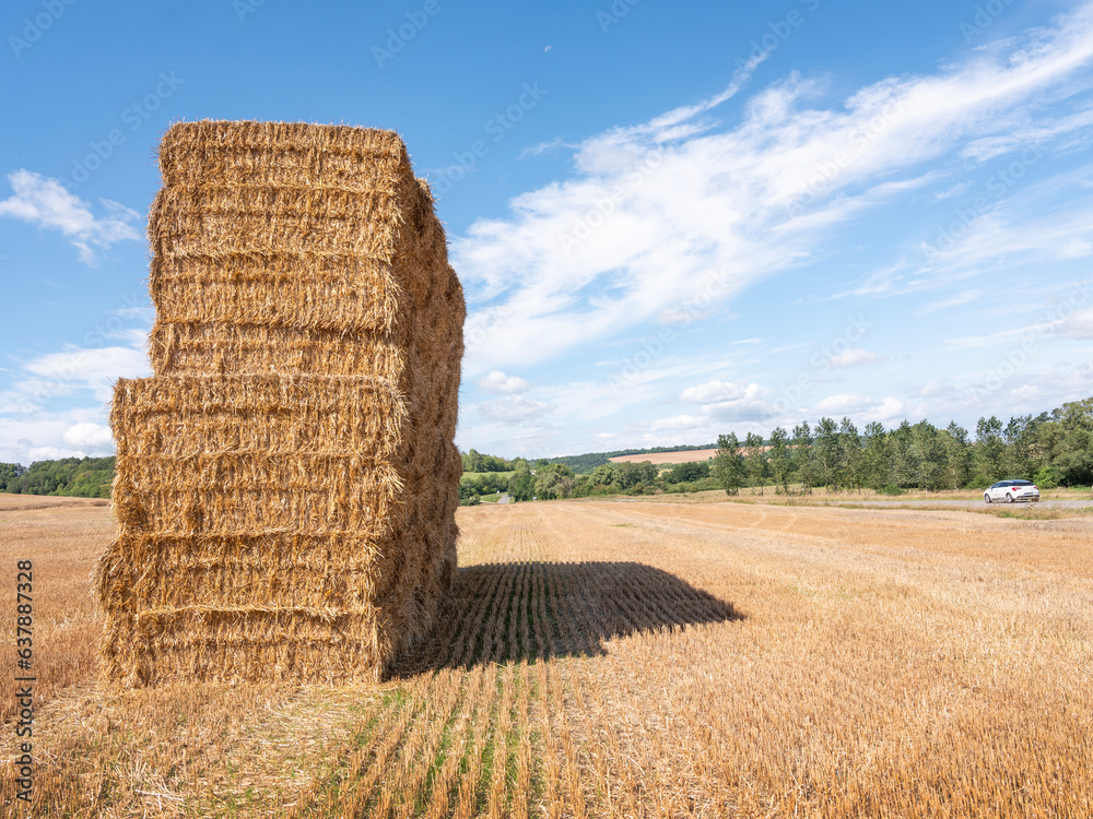 stack of straw bales in dry field and car on road in french lorraine