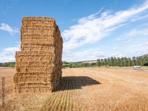 stack of straw bales in dry field and car on road in french lorraine