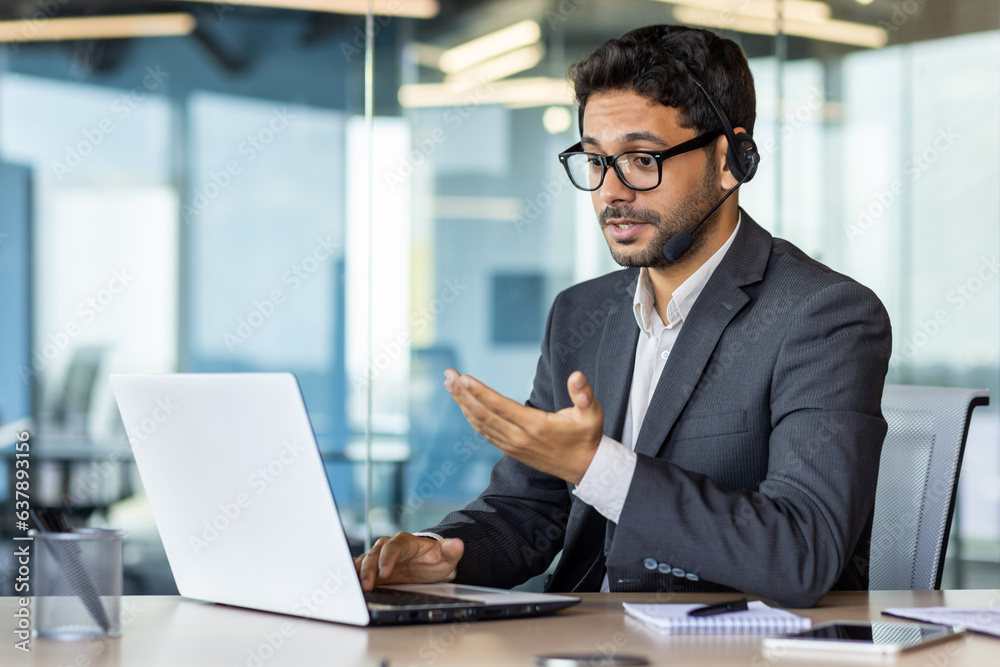 Serious concentrated and thinking businessman with headset phone for video call looking at web camera on laptop, man in business suit boss discreetly talking remotely with colleagues and partners. Serious concentrated and thinking businessman with headset phone for video call looking at web camera on laptop, man in business suit boss discreetly talking remotely with colleagues and partners.
