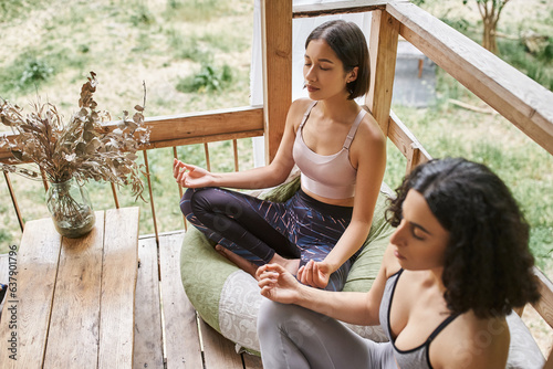 Photos young woman meditating in lotus pose near multiracial girlfriend in patio of ret