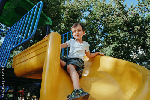 happy child kindergarten boy playing on slide on playground in summer © alexkoral