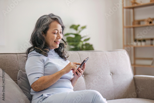Portrait, Happy 60s retired Asian woman using her phone on a sofa in the living room. chatting, scrolling on the phone