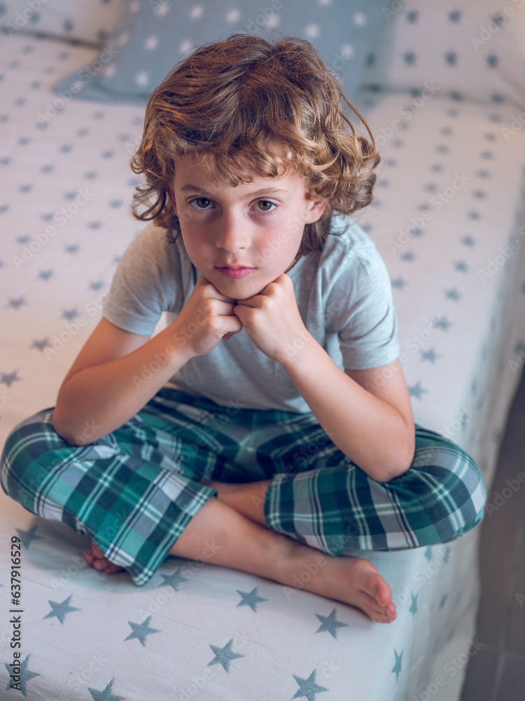 Cute boy in nightwear sitting with crossed legs on bed Cute boy in nightwear sitting with crossed legs on bed