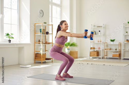 Portrait of sporty woman wearing sportswear doing sport exercises squatting with dumbbells at home. Athletic girl shaking leg muscles by doing sit-ups. Fitness, workout and home training concept.