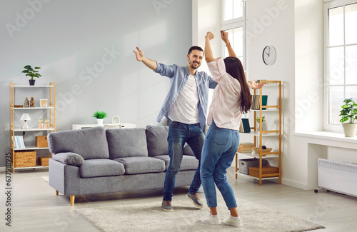 Happy family couple having fun together and dancing in the living room at home. Young man and woman celebrating something joyful like buying a new apartment or paying off mortgage early