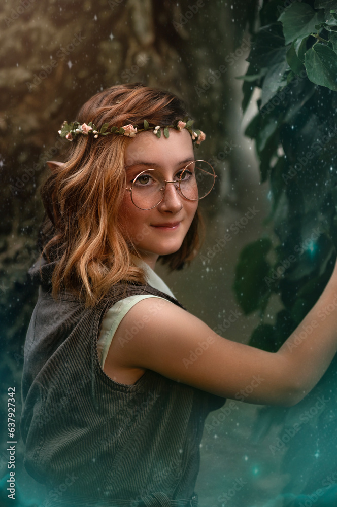 Fototapeta premium Fantasy elf girl in glasses in the fairy forest. Redhead fairy girl. Summer nature forest green tree. Red hair, pointy elf ears.