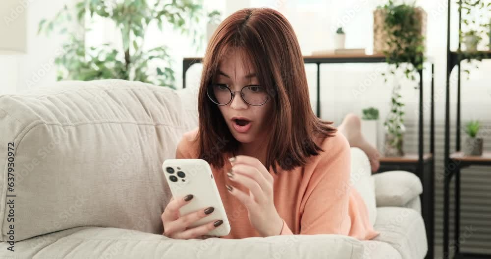 Lying on the couch, a teenage girl looks astonished as she engages in a conversation on her phone. Her fingers swiftly tap on the screen as she types out messages. Lying on the couch, a teenage girl looks astonished as she engages in a conversation on her phone. Her fingers swiftly tap on the screen as she types out messages.