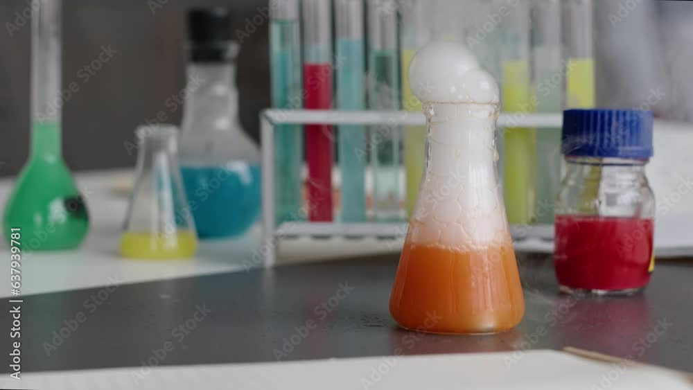 No people closeup of unrecognizable orange liquid bubbling and evaporating in glass flask during chemical experiment in school lab No people closeup of unrecognizable orange liquid bubbling and evaporating in glass flask during chemical experiment in school lab