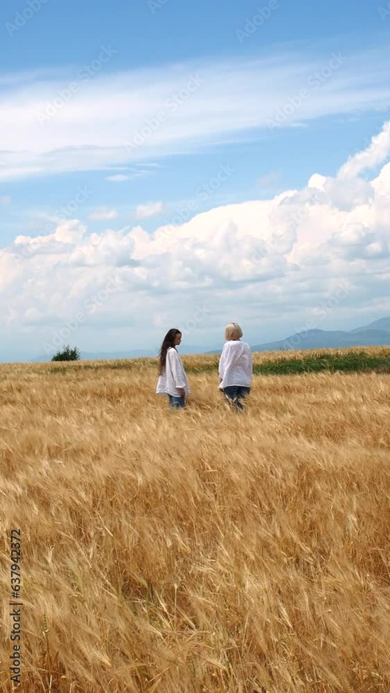 Two girls in white linen shirts and jeans walking in a rye field on a windy day Two girls in white linen shirts and jeans walking in a rye field on a windy day