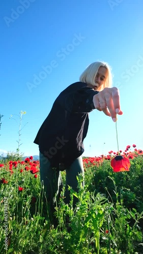 A girl with a flower in a poppy field dancing against a crystal clear blue sky