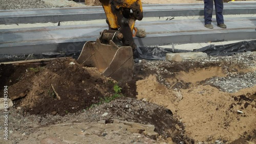 The yellow excavator bucket digs the ground during road works.