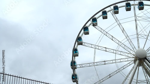 The ferris wheel is spinning slowly against the background of a cloudy sky.