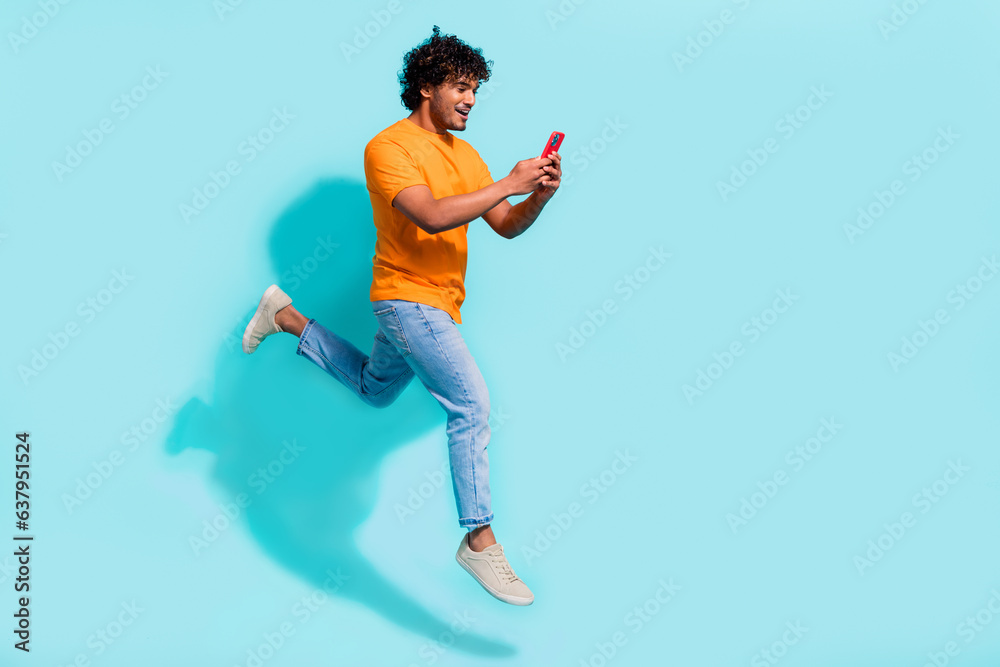 Fototapeta premium Full size profile portrait of crazy carefree guy jumping rush empty space use smart phone isolated on turquoise color background