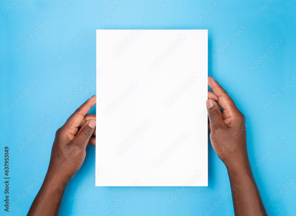Man holding a blank sheet of paper on blue background, top view Man holding a blank sheet of paper on blue background, top view