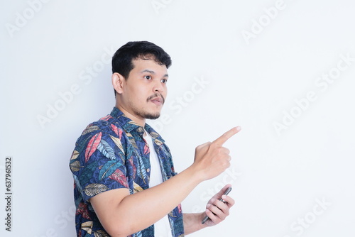 Adult Asian man wearing beach shirt looking to his phone while pointing to the right direction photo