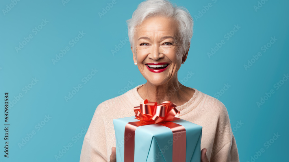Happy smiling senior woman holding gift box over blue background Happy smiling senior woman holding gift box over blue background