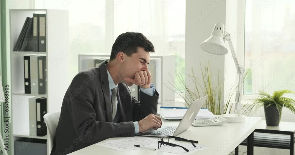 Tired Caucasian office worker is captured yawning while sitting at his desk. His facial expression reflects fatigue, and the yawn indicates the need for rest and rejuvenation. Tired Caucasian office worker is captured yawning while sitting at his desk. His facial expression reflects fatigue, and the yawn indicates the need for rest and rejuvenation.