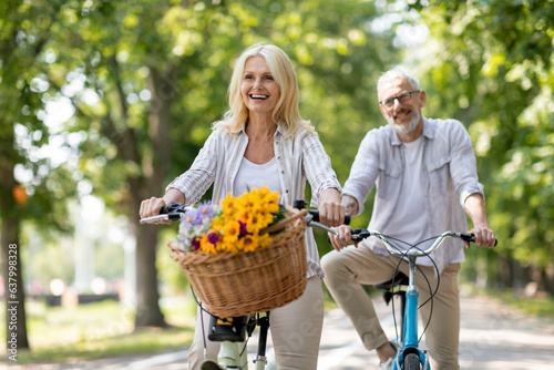 Happy cheerful mature couple enjoying bike ride in summer park photo