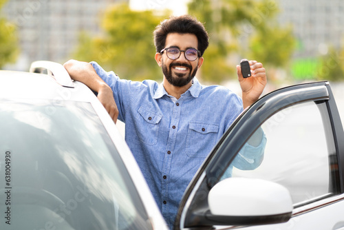 Cheerful millennial indian man driver holding key from auto