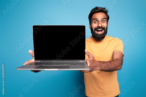 Great website. Excited middle aged indian man holding laptop computer with blank screen and exclaiming with joy, mockup