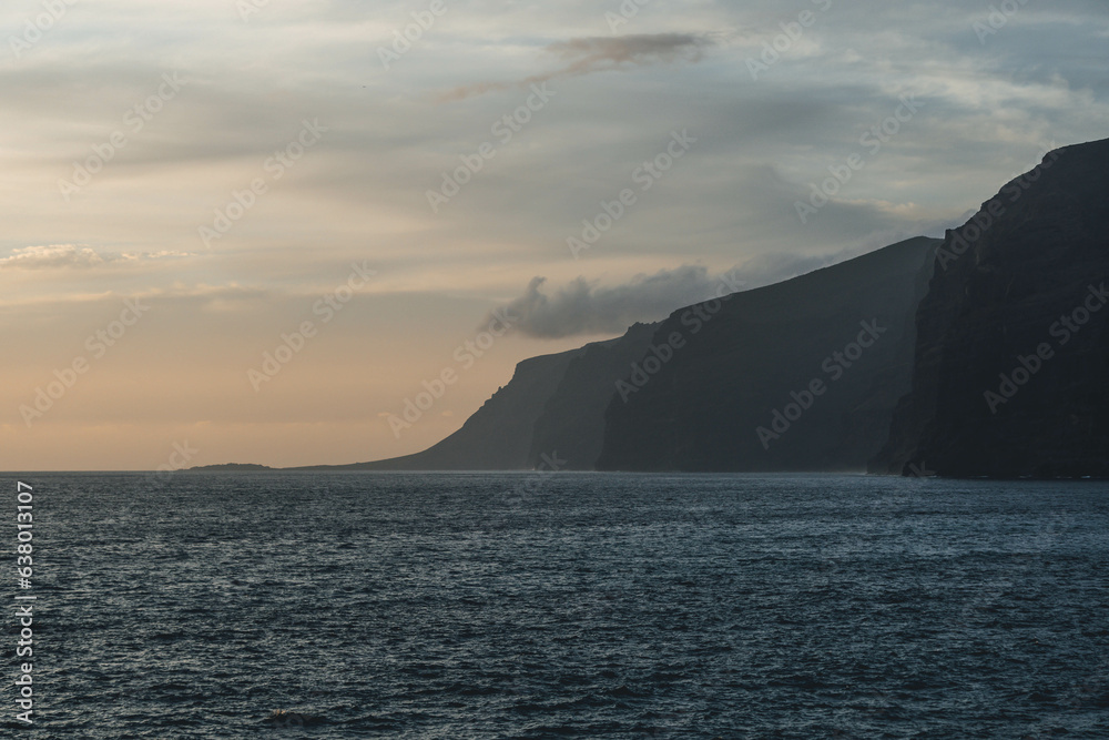 Sunset light with straight dark blue ocean waves and giant clifs hit by water