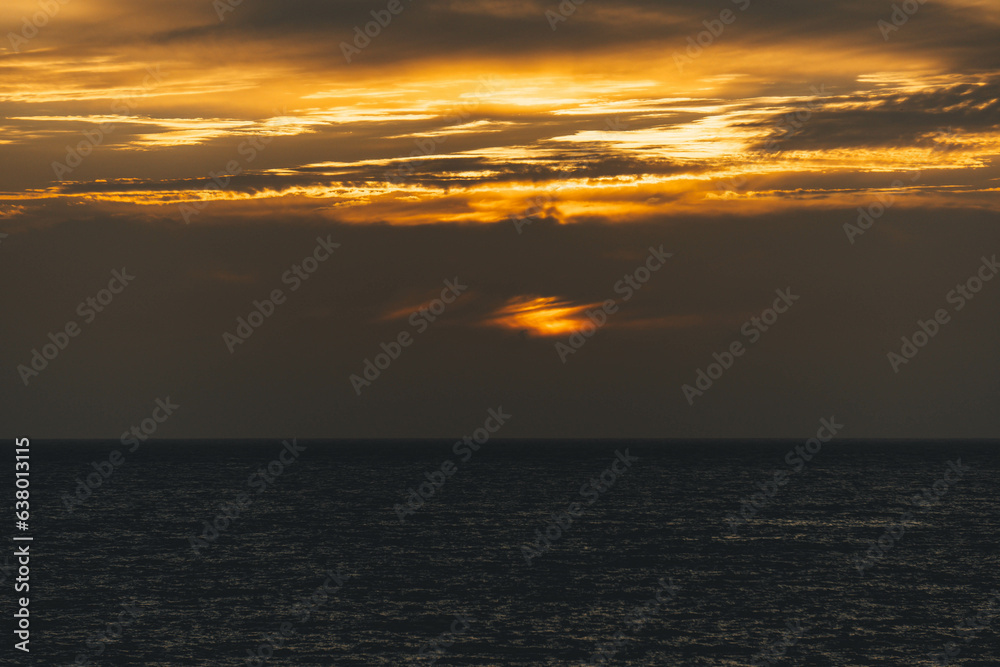 Sunset golden hour colors with grey clouds and sea horizon
