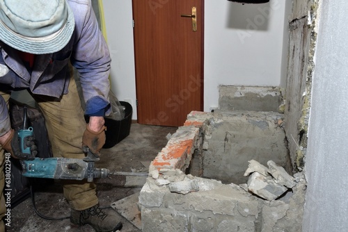 Obraz na płótnie A bricklayer uses a jackhammer to break a wall in a house while building a fireplace w salonie