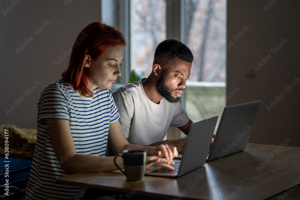 Serious man and woman working on laptops. Focused remote multiracial freelancer workers enthusiastically concentrate on online internet working at computer from home together jointly, typing. Serious man and woman working on laptops. Focused remote multiracial freelancer workers enthusiastically concentrate on online internet working at computer from home together jointly, typing.