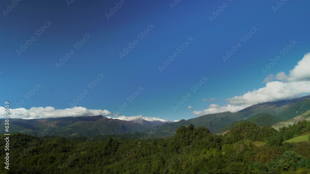 Landscape of mountain range covered by trees and green valleys under clear blue sky with flying clouds in timelapse. Scenery of cliffs and forest at warm summer day. Travel to Georgia and enjoy nature Landscape of mountain range covered by trees and green valleys under clear blue sky with flying clouds in timelapse. Scenery of cliffs and forest at warm summer day. Travel to Georgia and enjoy nature