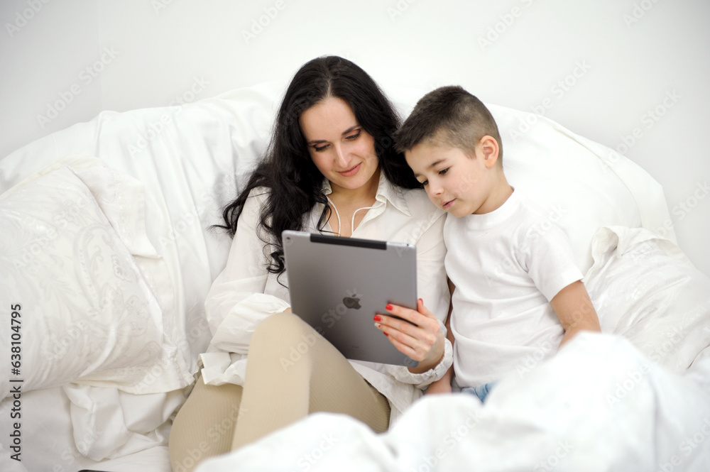 mom and son under blanket playing on tablet boy 4-6 years old woman with black hair beautiful lies under white sheet press buttons mom and son under blanket playing on tablet boy 4-6 years old woman with black hair beautiful lies under white sheet press buttons