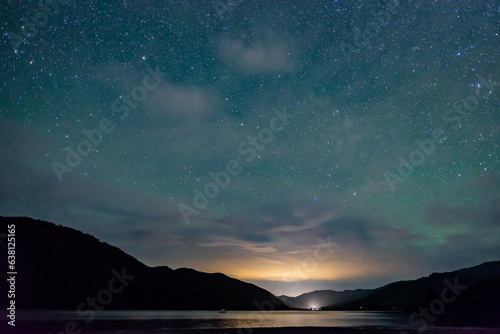 starry sky above the shape of mountains with the light of a city in a fjord in the Marlborough Sounds, New Zealand © ydumortier