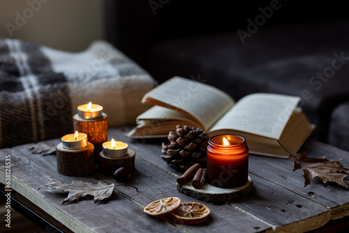 Cozy autumn or winter composition with aromatic candle, wool sweater, book. Aromatherapy, home atmosphere of cosiness and relax. Wooden background close up.