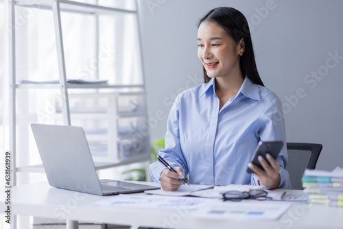 Business Asian woman working at office with phone on documents at her desk, doing planning analyzing the financial report, business plan investment, finance analysis concept 