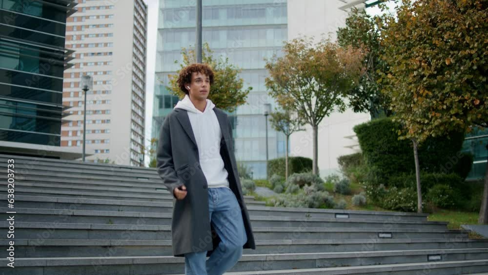 Relaxed teenager walking stairs at city street. Young man calling earphones Relaxed teenager walking stairs at city street. Young man calling earphones