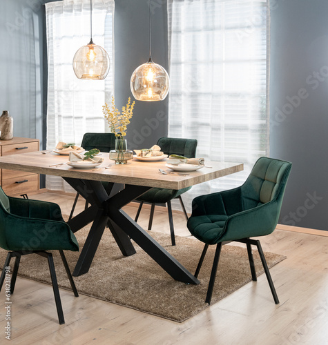 Modern dining room with tableware on a wooden table and a set of green chairs in Scandinavian style, against a gray neutral background