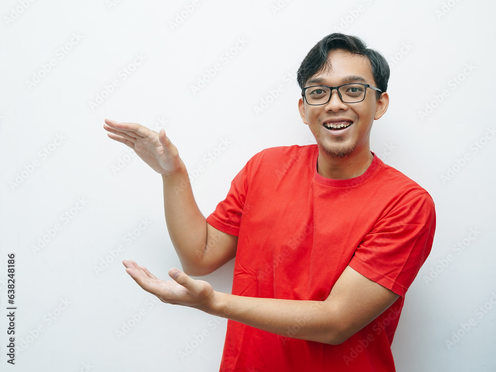 Portait of Young Asian man smiling while put hand palms in front of his body for presenting something. Red t-shirt for August 17 Indonesia independence day concept. Portait of Young Asian man smiling while put hand palms in front of his body for presenting something. Red t-shirt for August 17 Indonesia independence day concept.
